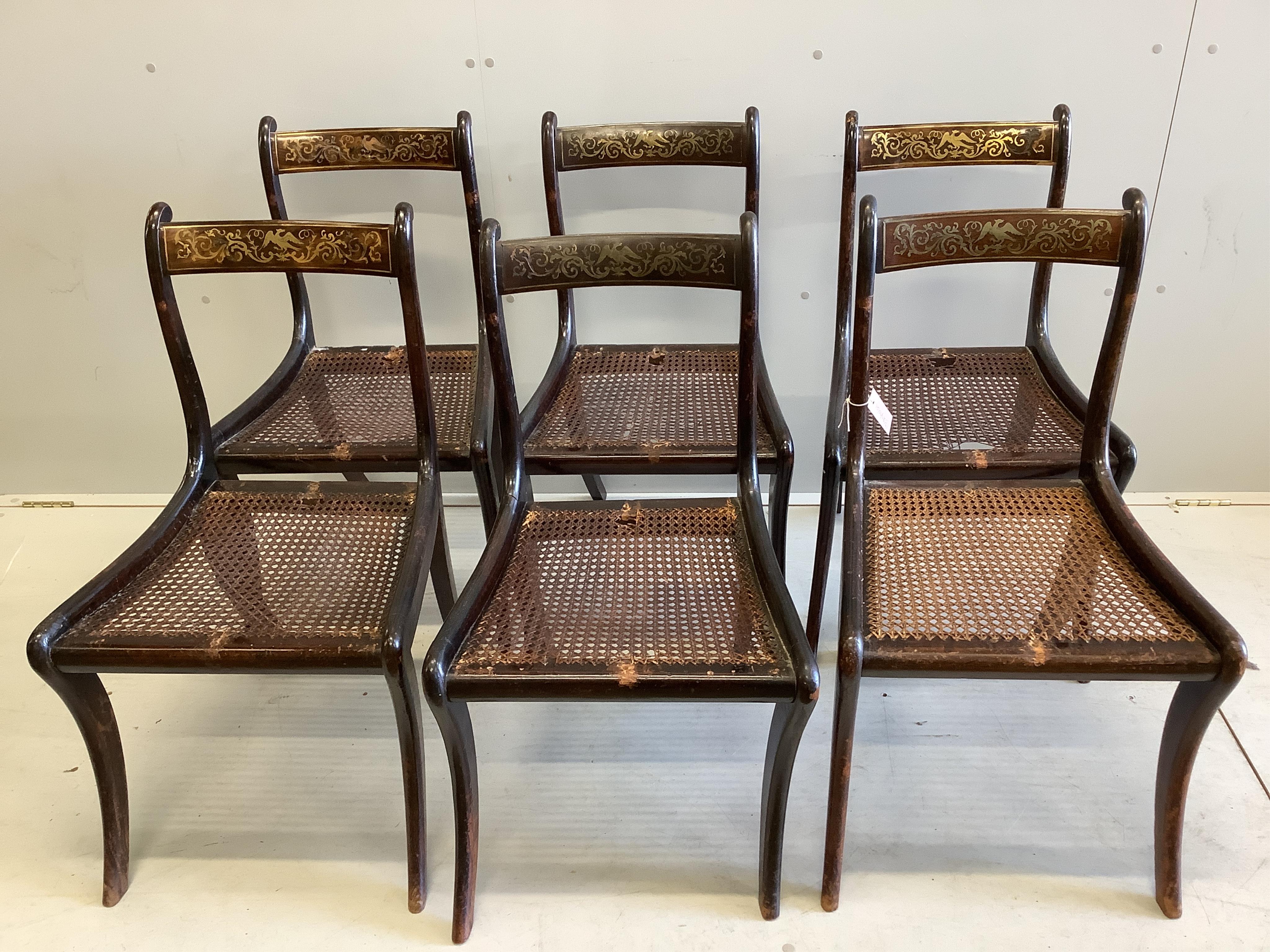 A set of six Regency rosewood and simulated rosewood dining chairs, the top rails inlaid with cut brass decoration, caned seats with slip-in cushions, on sabre legs. Condition - poor